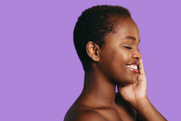 Close-up portrait of African woman, holding hand on cheek isolated over purple background with copy space. Skin care concept. New cosmetology product