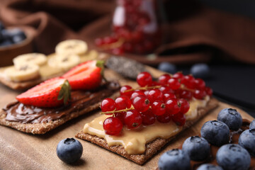 Fresh crunchy rye crispbreads with different toppings on wooden board, closeup