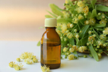 Bottle of essential oil and linden blossoms on white table