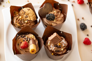 Chocolate cupcakes set on a white plate, chocolate decor and raspberries on a beige background.Choux pastry. Appetizing cupcakes and pastries.
