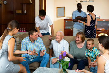 Big international family gathered together in parental home, cheerfully talking in living room