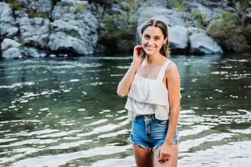 Beautiful blonde girl, using a white t-shirt and a blue denim short in a natural space, by the river. - obrazy, fototapety, plakaty