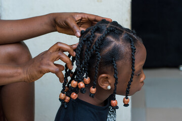 Hands of an african hair stylist or mother making braided hairstyle on the head of a little girl...