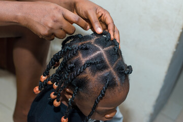 Hands of an african hair stylist or mother making braided hairstyle on the head of a little girl...