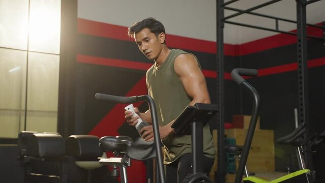 Asian handsome sportsman cleaning workout equipments in fitness club. 