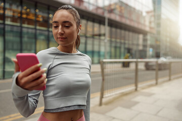 Young healthy sporty woman using cell phone during rest after jog. Blurred background