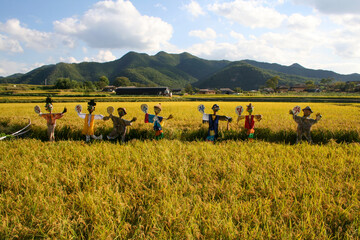 A line of colorful  traditional South Korean scarecrows in a field with moutains in the background.