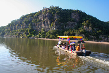 Naklejka premium A boat crosses a river approaching a small sandy beach at the base of a cliffside.