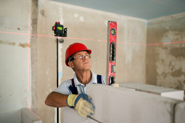 Bricklayer using spirit bubble and laser level to precise check concrete blocks on wall. Contractor...