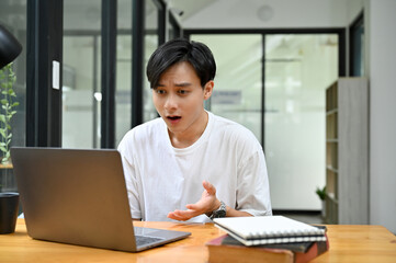 Stunning young Asian male college student or freelancer looking at laptop screen.