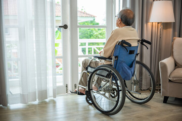 Fototapeta na wymiar Asian senior man disabled sitting alone in wheelchair looking through window at hospital, lonely elder thoughtful sad old man look outside windows in bedroom at retirement home, feel depressed lonely