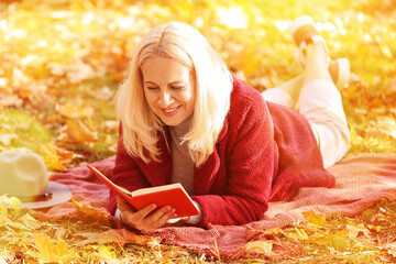 Mature woman reading book on plaid in autumn park