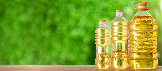 Bottles of sunflower oil on table against blurred green background with space for text
