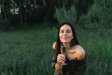 An attractive woman with a glass of champagne on a forest plot in the middle of nature. Front view.