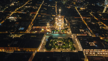 the church Parroquia Archangel Jardin Town Square Night Tree Decoraciones San Miguel de Allende, México. Parroaquia. Night and morning light in a drone view.