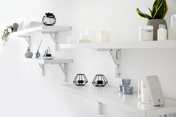 White shelves with bath supplies, candles and houseplant hanging on light wall