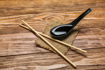 Spoon of soy sauce, chopsticks and sack cloth on wooden background