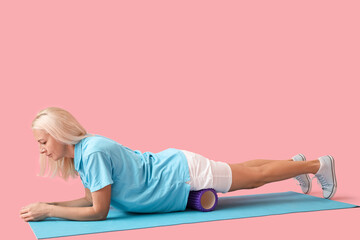 Mature physiotherapist training with foam roller on pink background