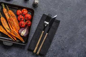 Fototapeta na wymiar Baking dish with tasty baked vegetables and cutlery on dark background