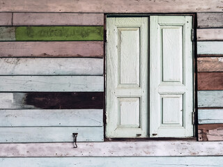 Obraz na płótnie Canvas Old grunged wooden window frame painted white vintage with old colourful plywood wall. Antique window frame and old panes. Old closed window and planks of old wooden house. Background of wooden walls
