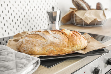 Baking sheet with fresh bread on stove in kitchen