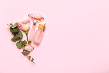 Facial massage tool with cosmetic bottle, eucalyptus and rose on pink background