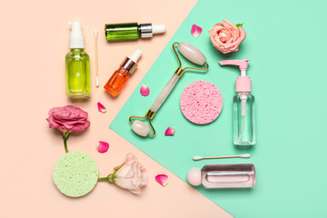 Facial massage tool with cosmetic products and flowers on color background