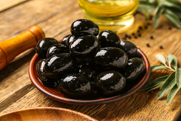 Plate of tasty black olives on wooden table, closeup