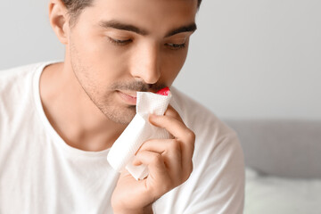 Young man wiping nosebleed with tissue at home, closeup
