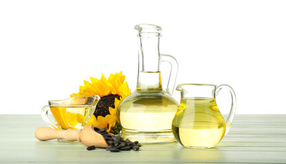 Glass containers with sunflower oil and seeds on color wooden table against white background