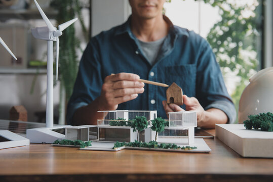 Architect designer making modern home office model for living using natural energy concept, natural light and green tree around, with wind turbine model and solar panels. Focus shoot at home model.