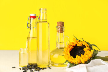 Bottles of sunflower oil on table against yellow background
