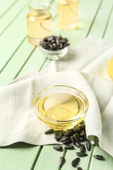 Bowl of oil with sunflower seeds and napkin on green wooden background, closeup