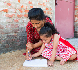 Mother teaching Hindi to daughter on her lap. Homeschooling, Happy teacher day and promote Hindi Diwas concept. selective focus. 