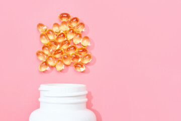 Scattered vitamin D capsules and a white bottle on a pink background close-up, copy space.