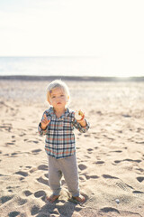 Little girl in a tracksuit with an apple in her hand stands on the sand. High quality photo