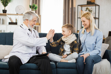 Fototapeta Mature man doctor giving high five during home visit of sick preschool boy patient sitting with mom, medical history or anamnesis, medical insurance contract. obraz