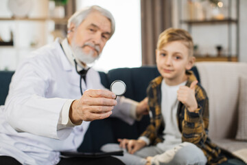 Close up of sick child boy sitting on the couch showing thumb up, while caring confident mature...