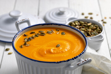 Yellow cream soup in the white dish on the white wooden table, close-up view