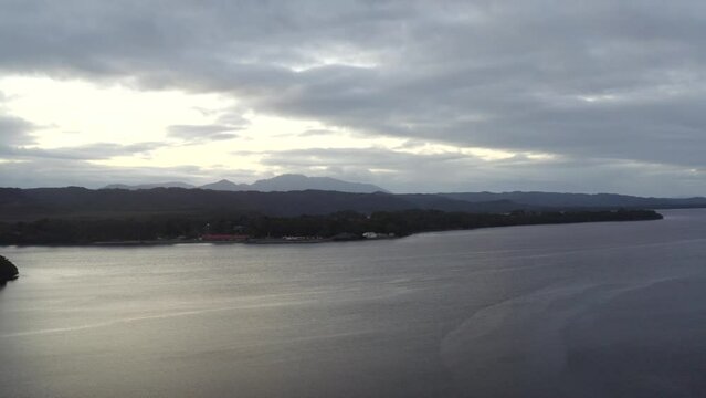 Aerial: Drone flying over a large lake towards the mountains on the horizon near Strahan, Australia