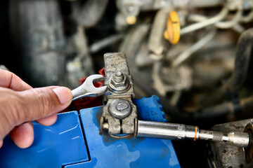 hand holding a wrench on car battery.