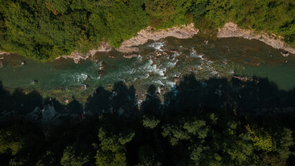Mountain emerald river with stone coast and forest, strong stream with twists of crystal clear mountain river. Aerial drone top down view at summer sunny day