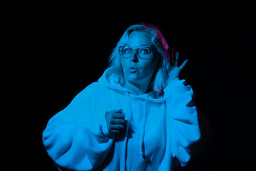 curious woman in glasses in a hoodie eavesdrops in blue light on a black background