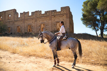Young and beautiful Spanish woman on a Thoroughbred horse riding in the countryside in Spain. The...
