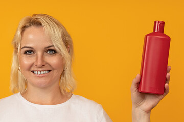 blond woman smiling and showing shampoo bottle against colored background