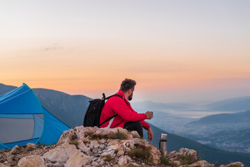 A happy traveler relaxing while drinking a cup of coffee near tent camping during the hiking on the mountain.	