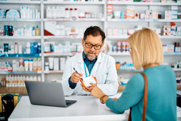 Mature pharmacist advising female customer who is buying prescription medicine in pharmacy.
