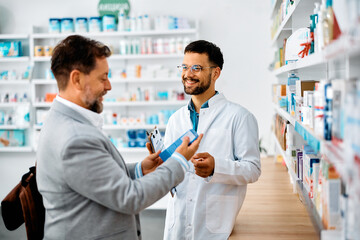 Happy pharmacist assists his customer in choosing products in pharmacy.