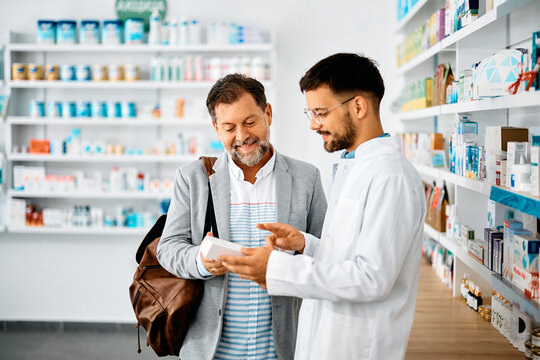 Happy man chooses medicine with help of young pharmacist in drugstore.