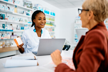 Happy black pharmacist advising senior woman in buying medicine in drugstore.
